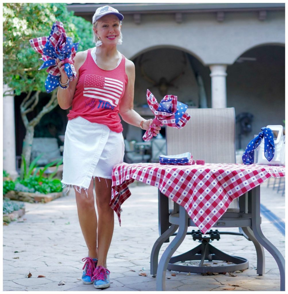 Sheree of the SheSheShow standing outside decorating for the 4th of july wearing white denim skirt and red flag t shirt