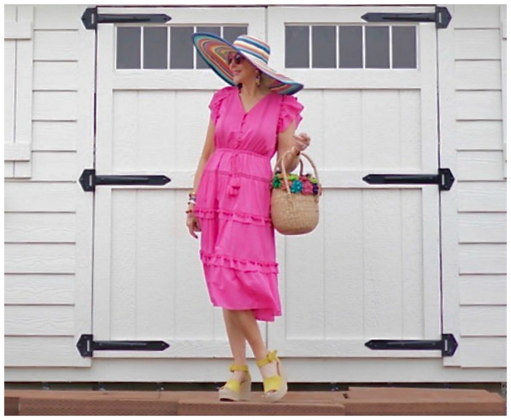 Sheree Frede of the SheShe Show standing in front of a white door wearing a hot pink dress and large hat