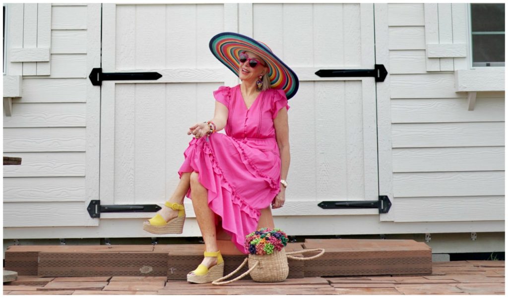 Sheree Frede of the SheShe Show sitting in front of a white door wearing a hot pink dress and large hat