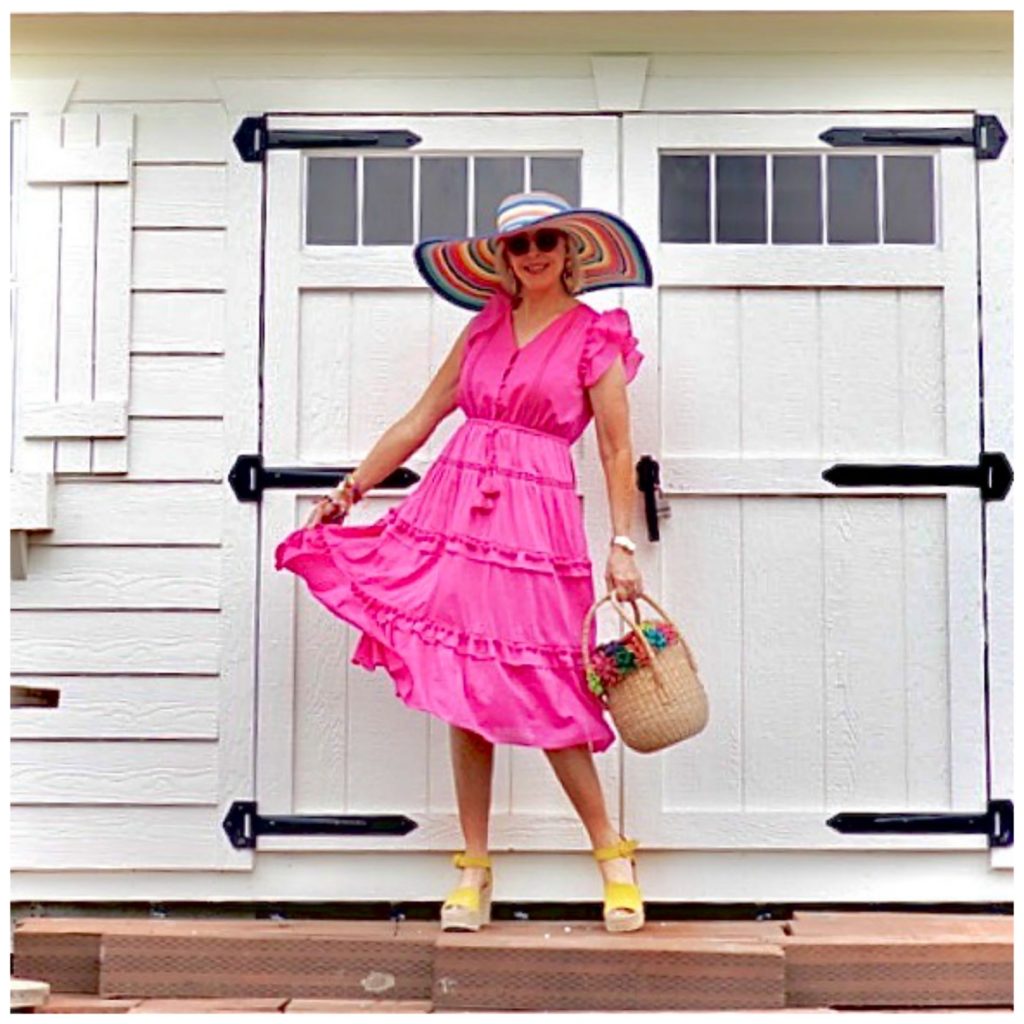 Sheree Frede of the SheShe Show standing in front of a white door wearing a hot pink dress and large hat