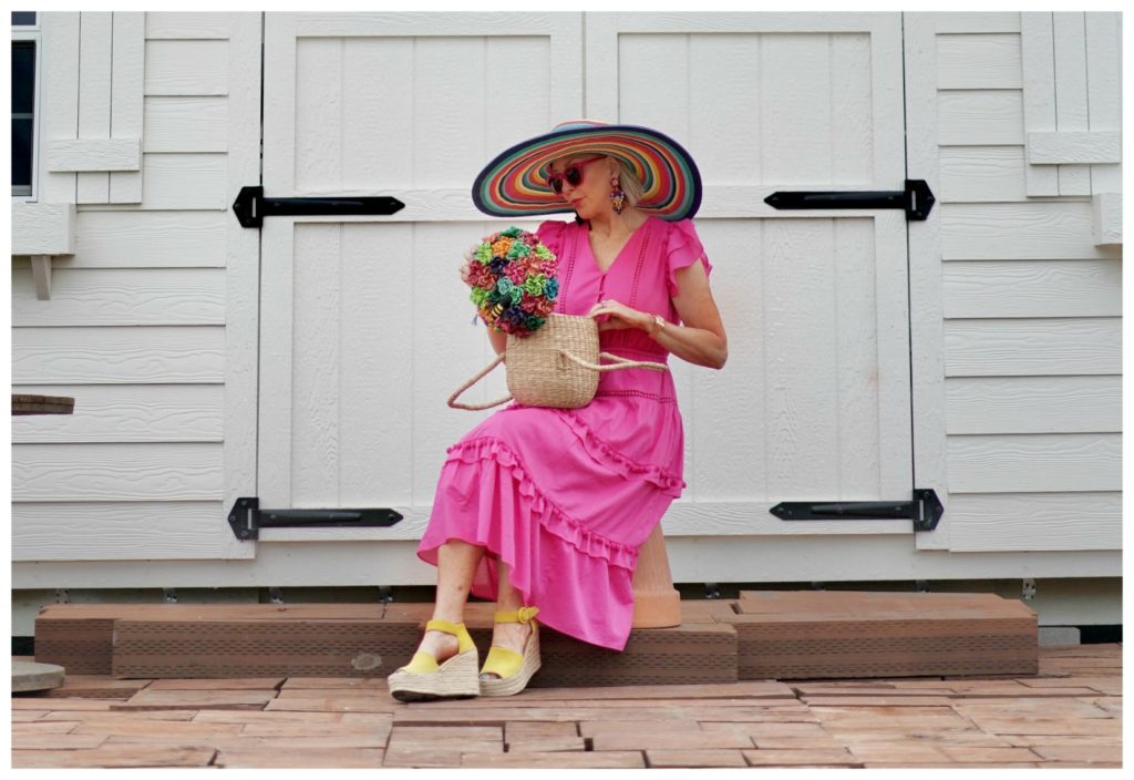 Sheree Frede of the SheShe Show sitting in front of a white door wearing a hot pink dress and large hat