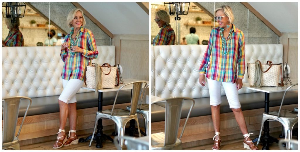 Sheree Frede of the SheShe SHow standing in a restaurant wearing a plaid shirt, white shorts, straw bag.