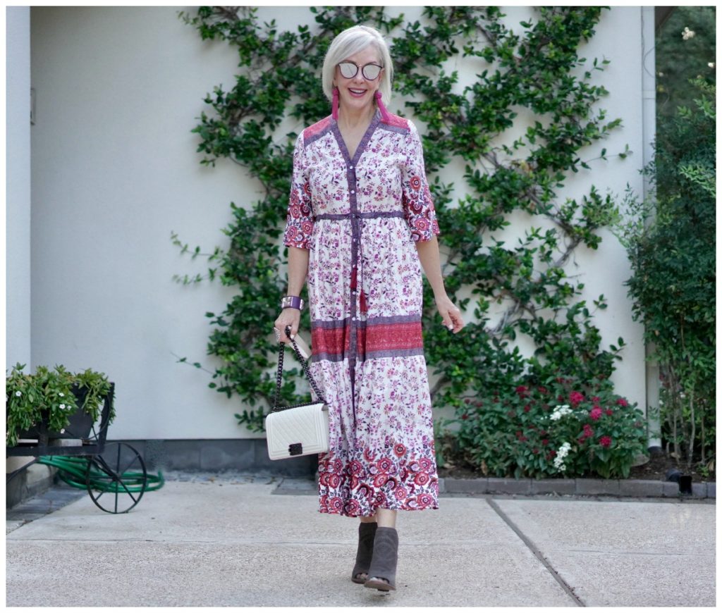 Sheree Frede of the SheSheShow standing in front of trellis wall wearing a maxi red and white floral dress