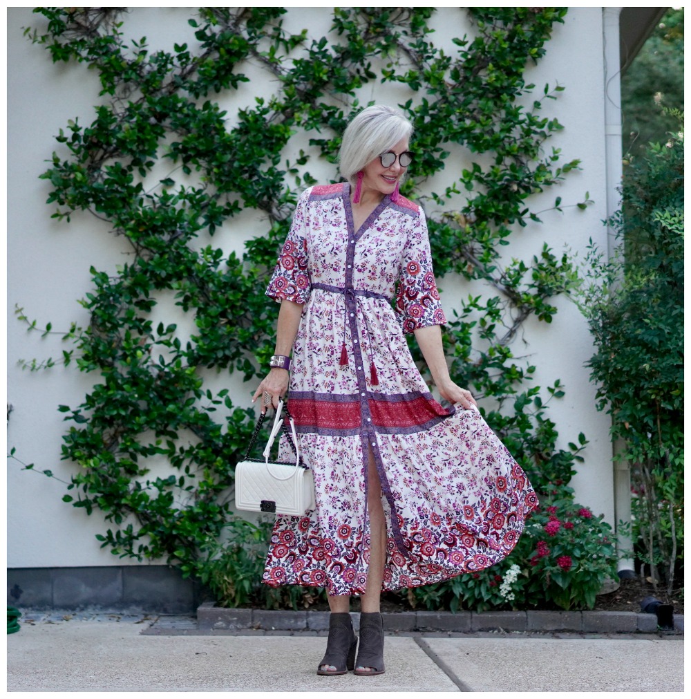 Sheree Frede of the SheSheShow standing in front of trellis wall wearing a maxi red and white floral dress