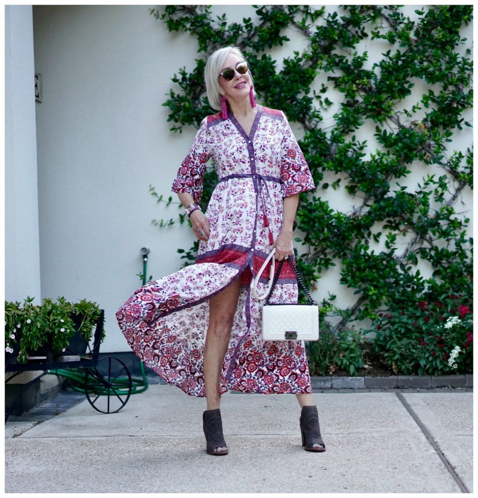 Sheree Frede of the SheSheShow standing in front of trellis wall wearing a maxi red and white floral dress