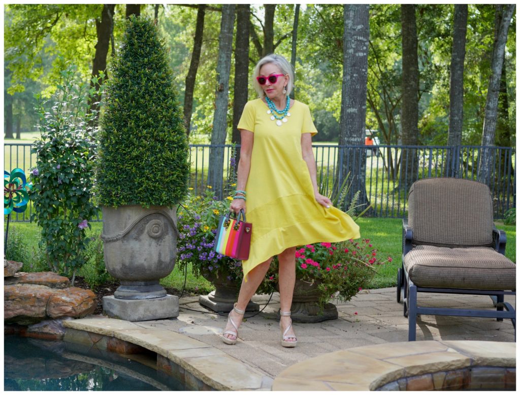 Sheree Frede of the SheShe Show stand in a flower garden wearing a yellow dress