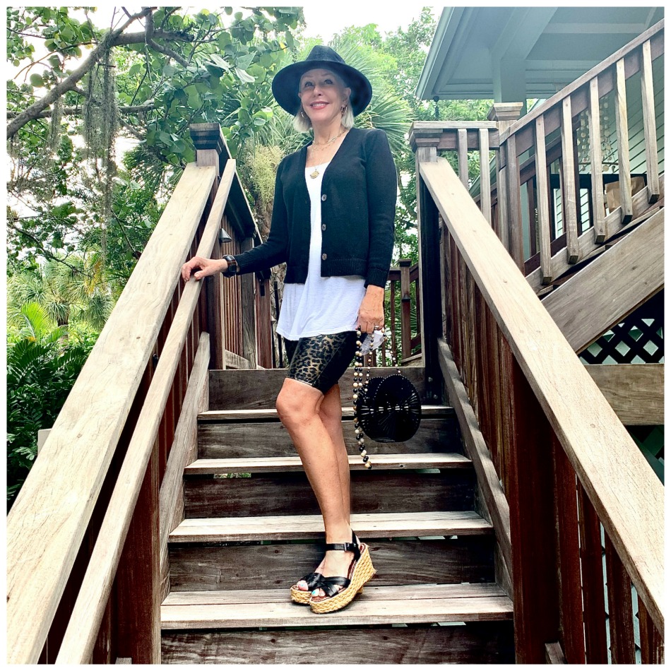 Sheree Frede of the SheShe Show walking up outdoor wooden stairs wearing bike shorts and black cardigan with black hat