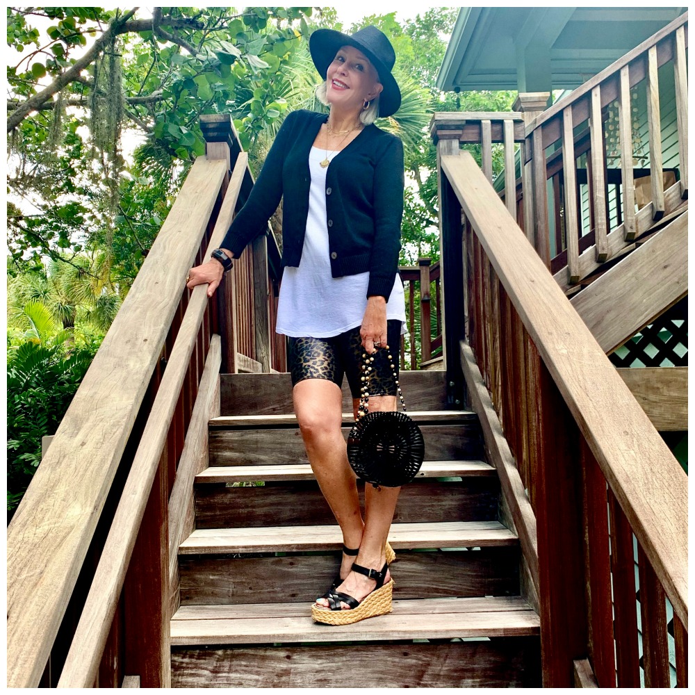 Sheree Frede of the SheShe Show walking up outdoor wooden stairs wearing bike shorts and black cardigan with black hat