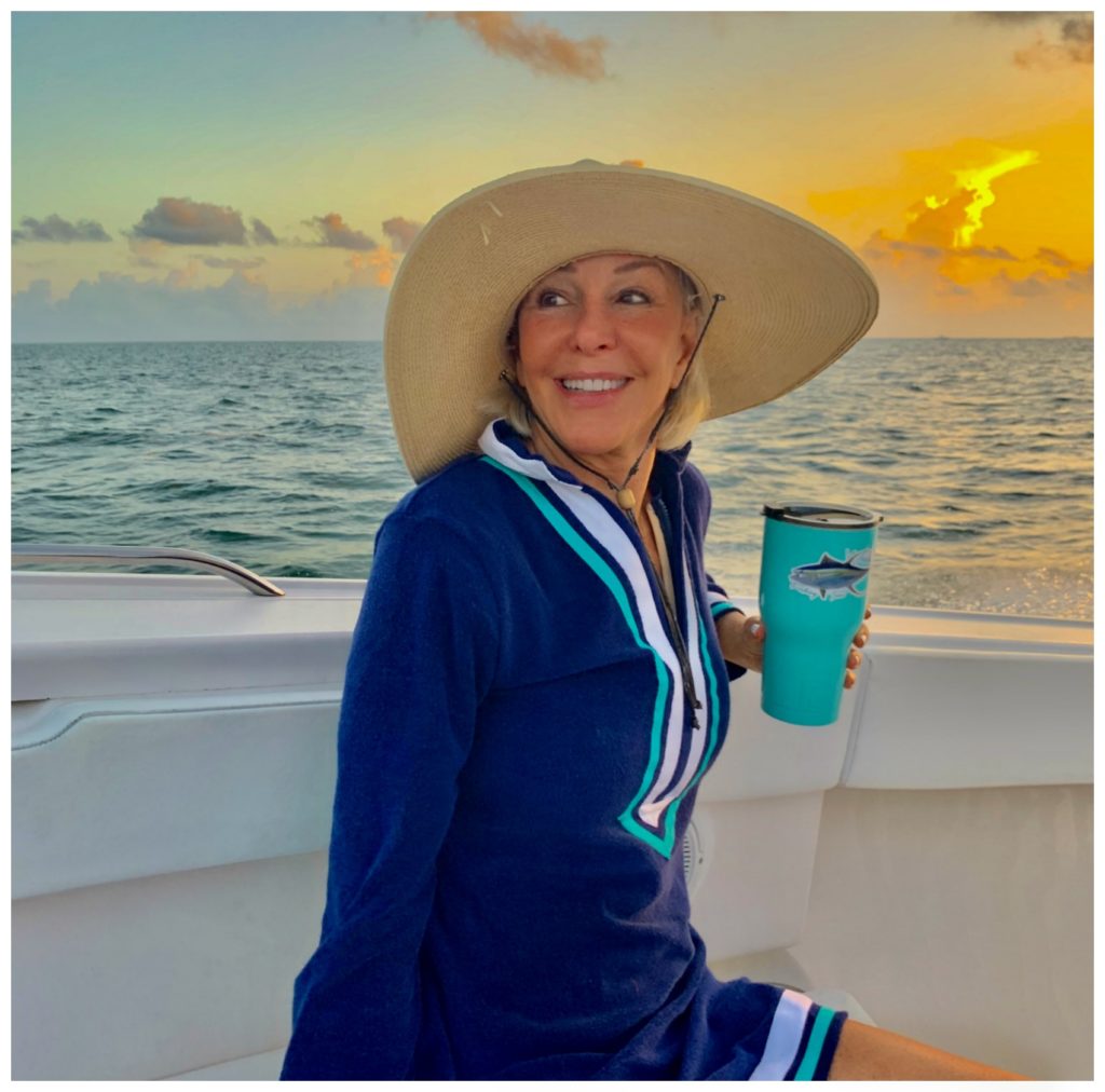 Sheree Frede of the SheShe Show sitting on the bow of a small fishing boat wearing a navy Cabana life swimsuit coverup