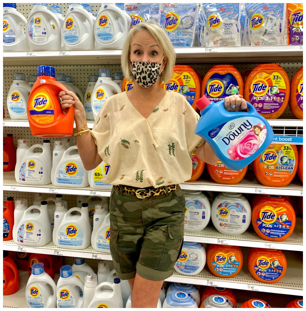 Sheree Frede of the SheShe Show wearing camo shorts standing in the laundry aisle at Target holding Tide and Downy