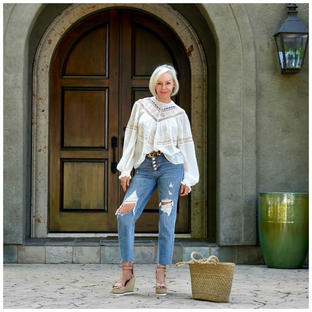 Sheree Frede of the SheShe Show in front of big wood door wearing ripped jeans and an off white victorian top