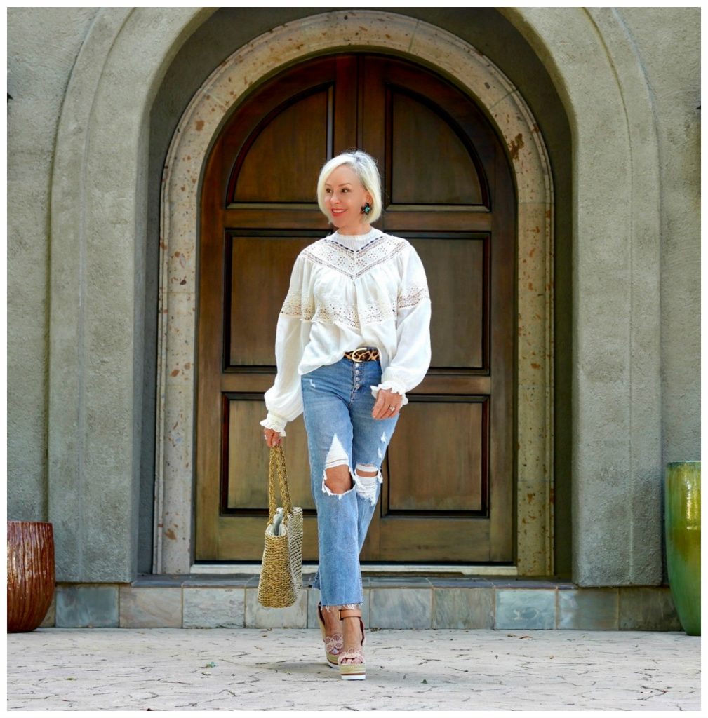 Sheree Frede of the SheShe Show in front of big wood door wearing ripped jeans and an off white victorian top