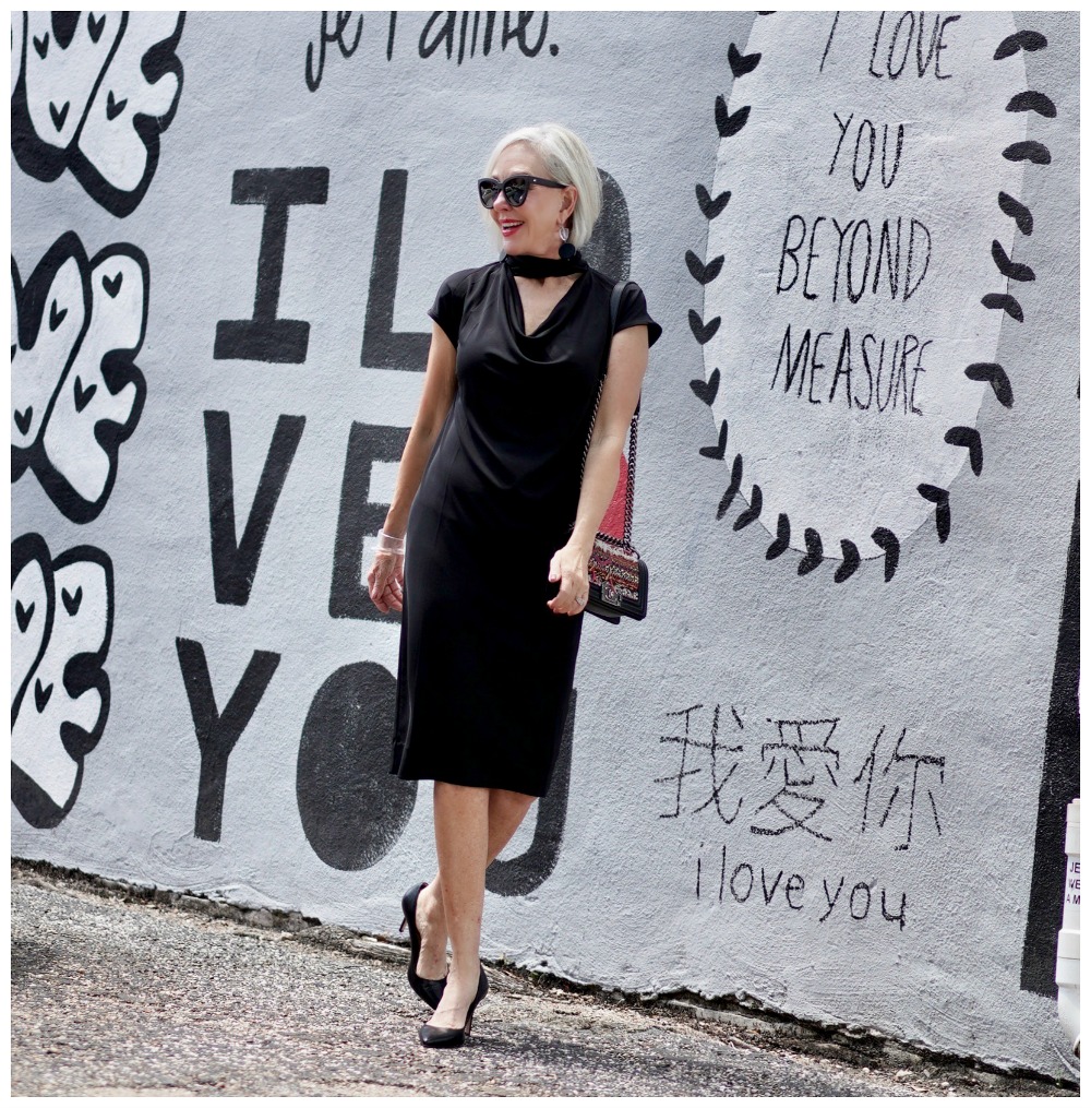 Sheree Frede of the SheShe Show standing in front of mural wall wearing a Chicos black shift dress
