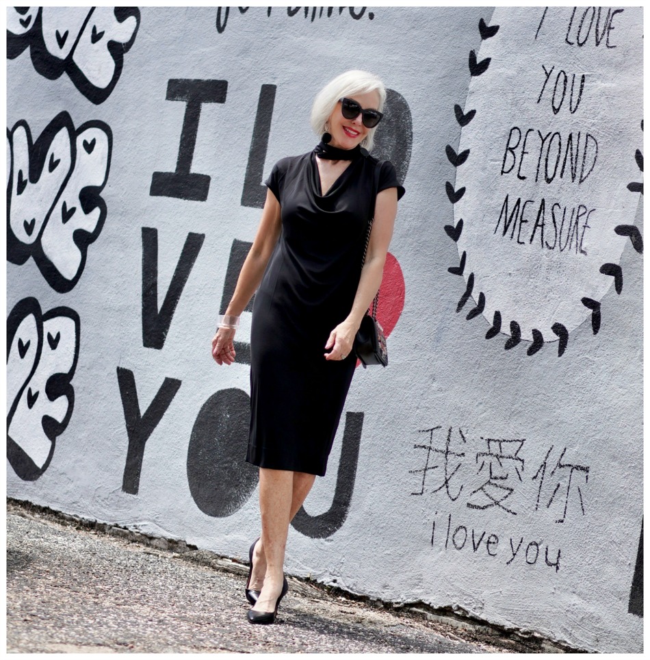 Sheree Frede of the SheShe Show standing in front of mural wall wearing a Chicos black shift dress