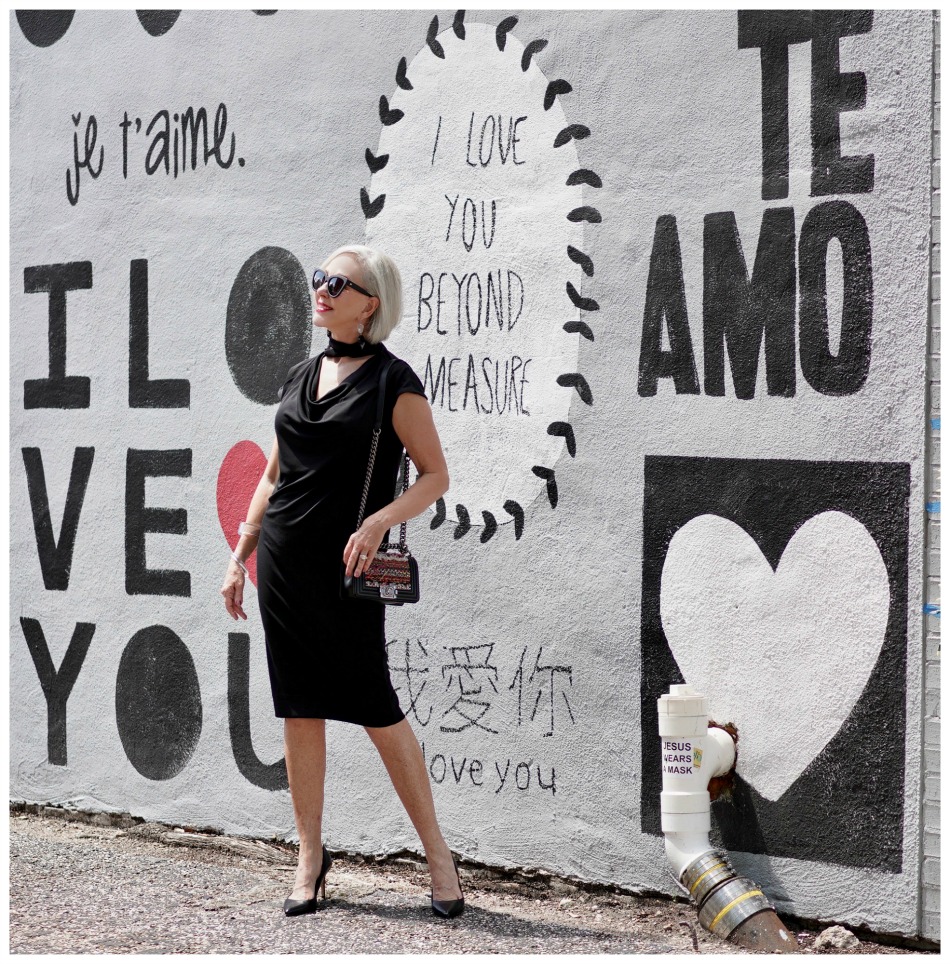 Sheree Frede of the SheShe Show standing in front of mural wall wearing a Chicos black shift dress