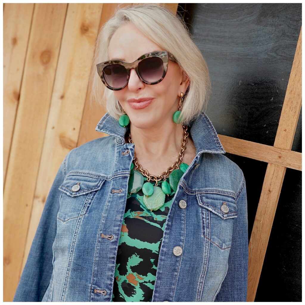 Sheree Frede of the SheShe Show walking in front of a cedar sided house wearing a green leopard print dress with denim jacket