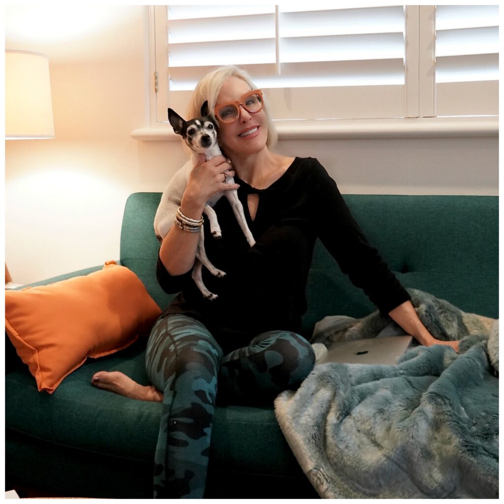 Sheree Frede of the SheShe Show sitting on turquoise sofa with her white toy fox terrier wearing green leopard leggings and black top