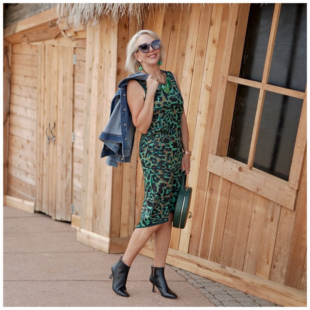 Sheree Frede of the SheShe Show walking in front of a cedar sided house wearing a green leopard print dress with denim jacket