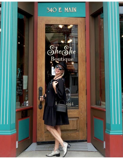 Sheree Frede of the SheSheShow standing in front of a door wearing an above the knee black dress