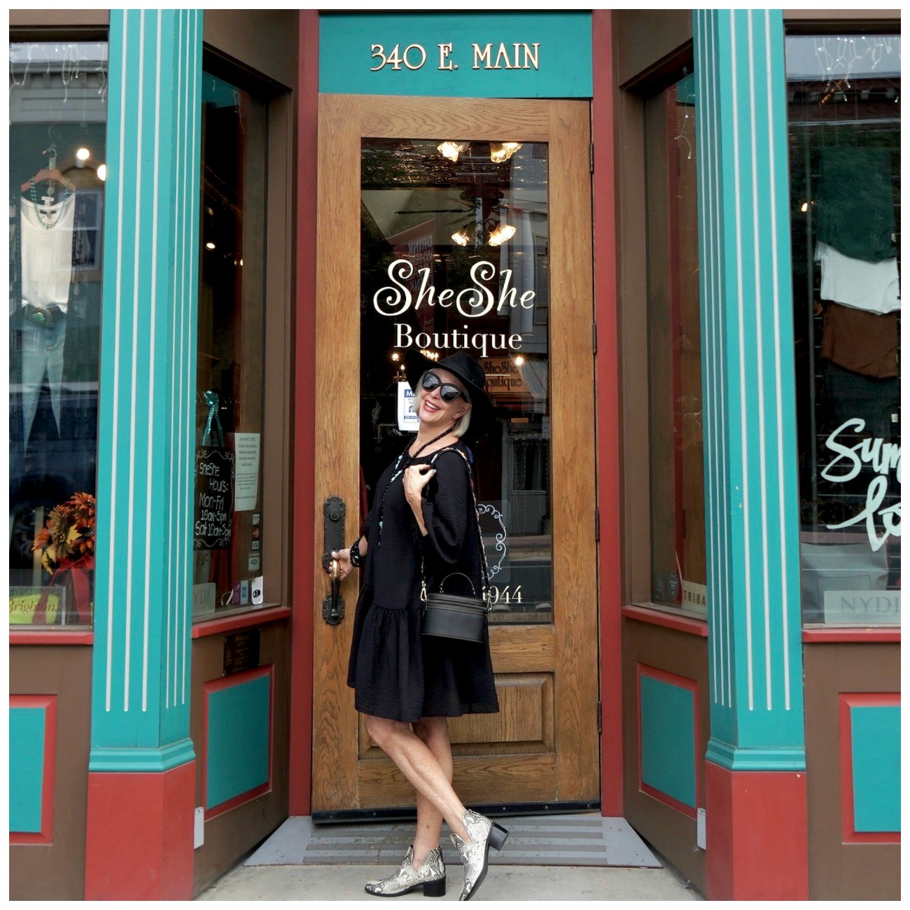 Sheree Frede of the SheSheShow standing in front of a door wearing an above the knee black dress