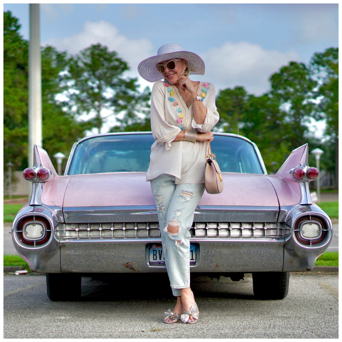 Sheree Frede of the SheShe Show standing by pink cadillac wearing ripped jeans and tassel top
