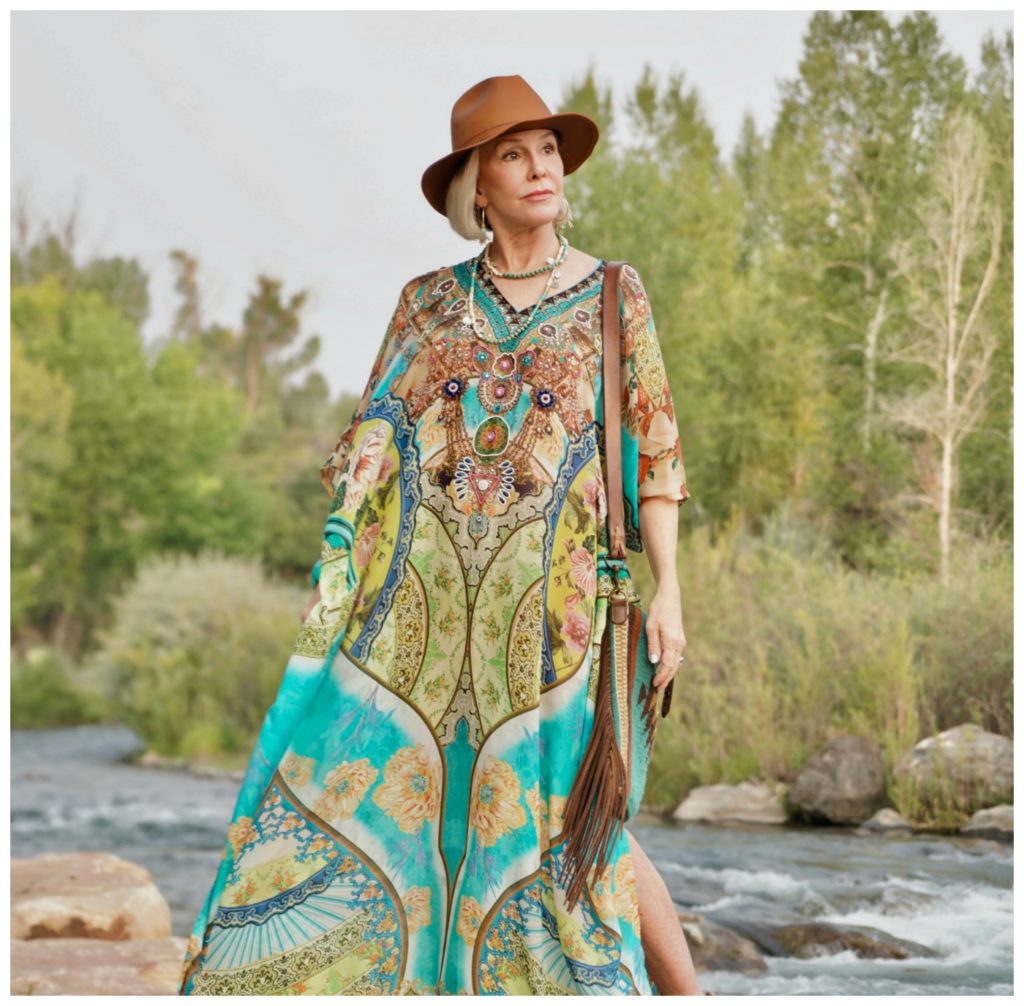 Sheree Frede of the SheShe Show standing by the river wearing a turqoise and rust print kaftan with leather hat.