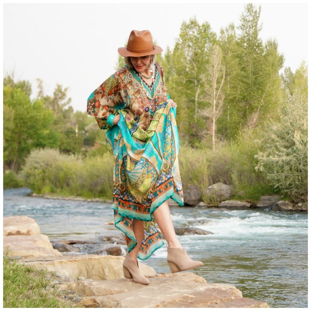 Sheree Frede of the SheShe Show standing by the river wearing a turqoise and rust print kaftan with leather hat.