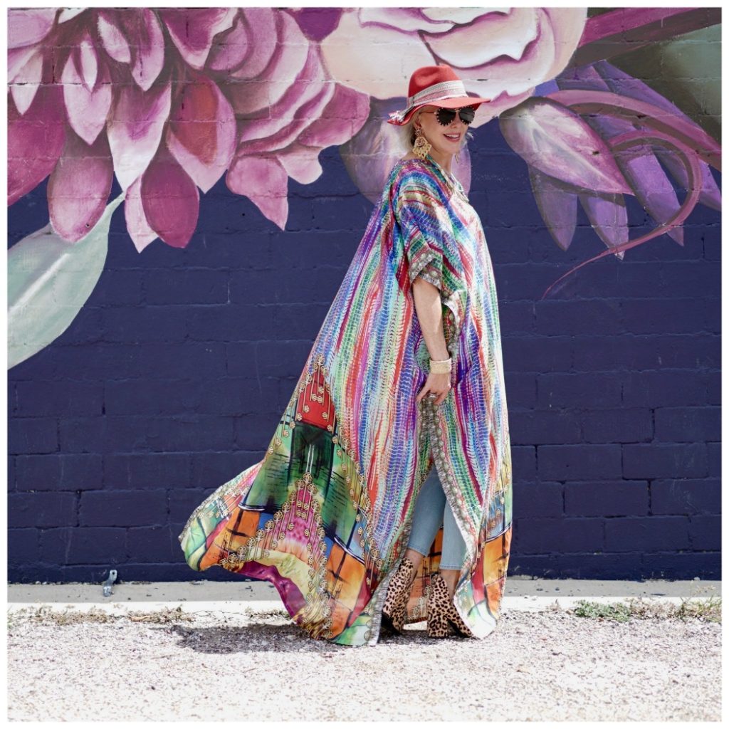 Sheree Frede of the SheShe Show walking in front of purple floral mural wearing a purple, green and orange print silk kaftan