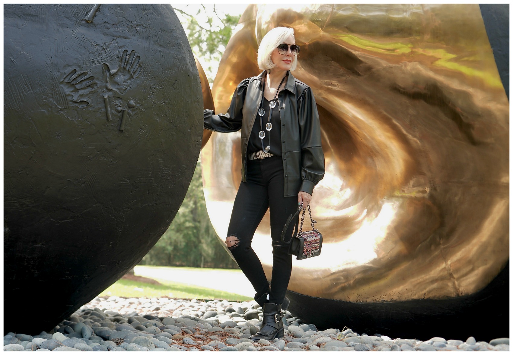 Sheree Frede of the SheShe Show standing in front of an outdoor sculpture wearing a black faux leather shirt and jeans