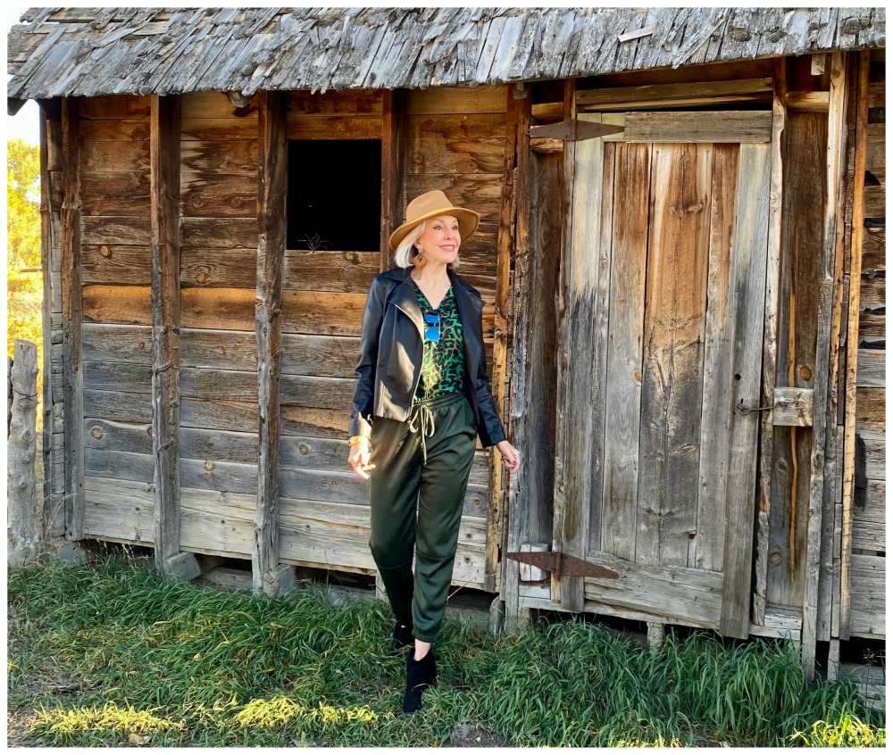 Sheree Frede of the SheShe Show standing in front of old barn wearing green satin jogger pants and leather bomber jacket