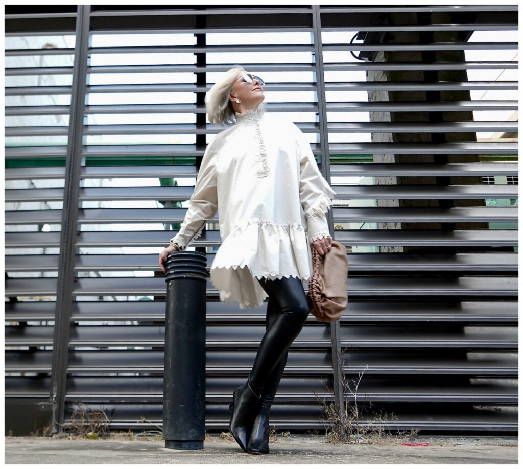 Sheree Frede of the SheShe Show posing in front of grid wearing a white balloon tunic over faux leather leggings