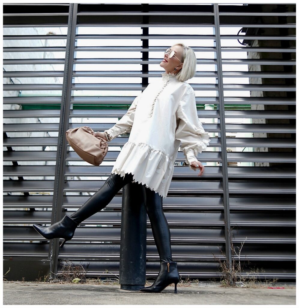 Sheree Frede of the SheShe Show posing in front of grid wearing a white balloon tunic over faux leather leggings