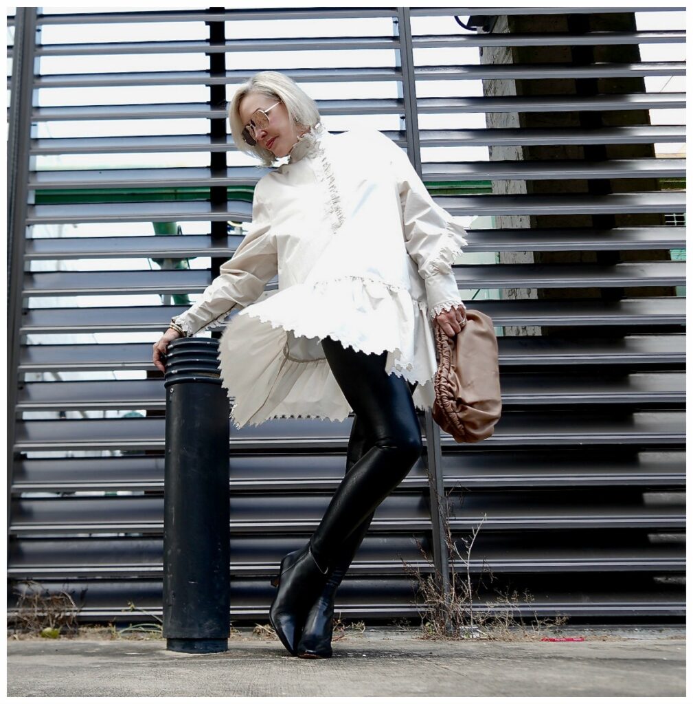 Sheree Frede of the SheShe Show posing in front of grid wearing a white balloon tunic over faux leather leggings