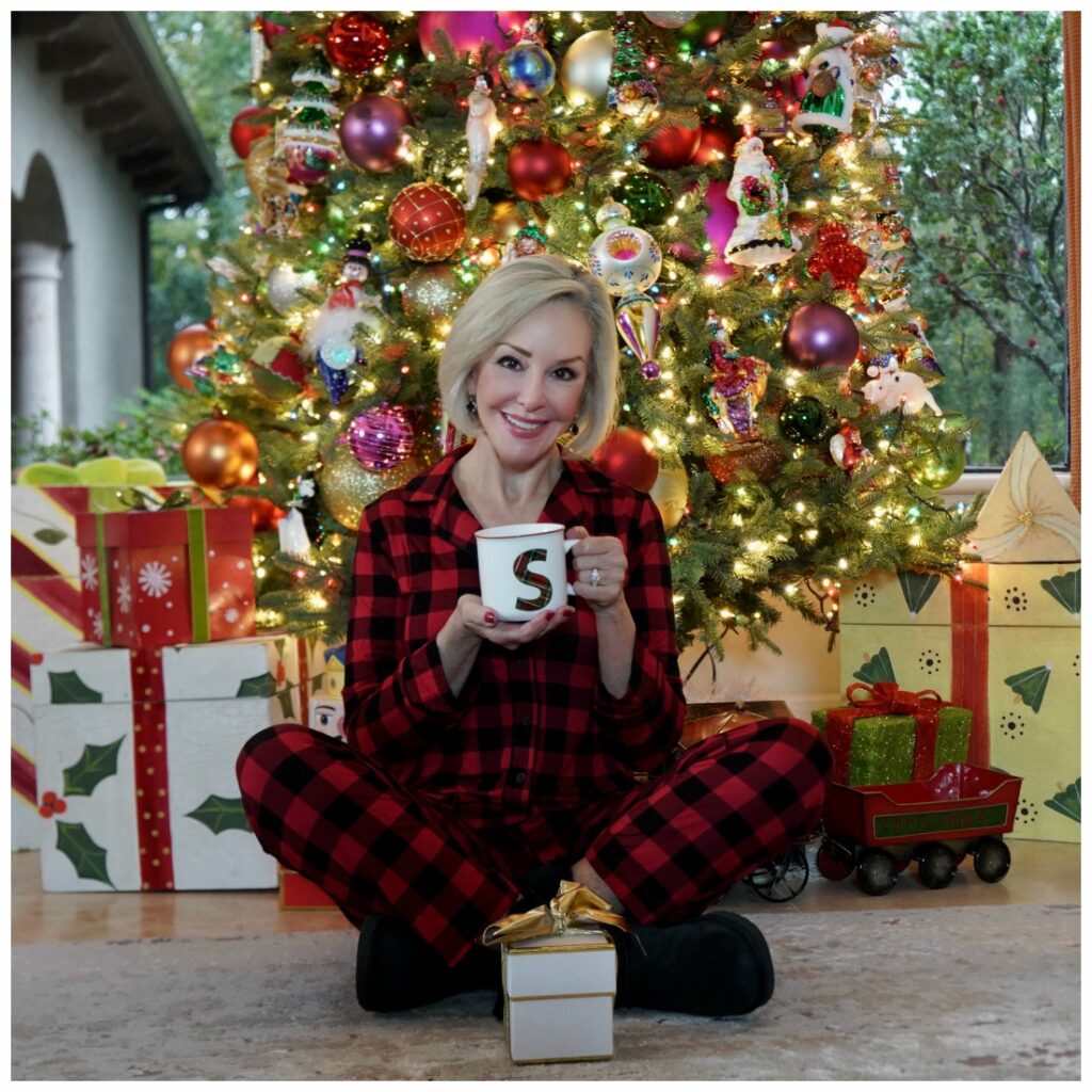 Sheree Frede of the SheShe Show sitting in front of Christmas tree holding a coffee mug, wearing red and black plaid pajamas
