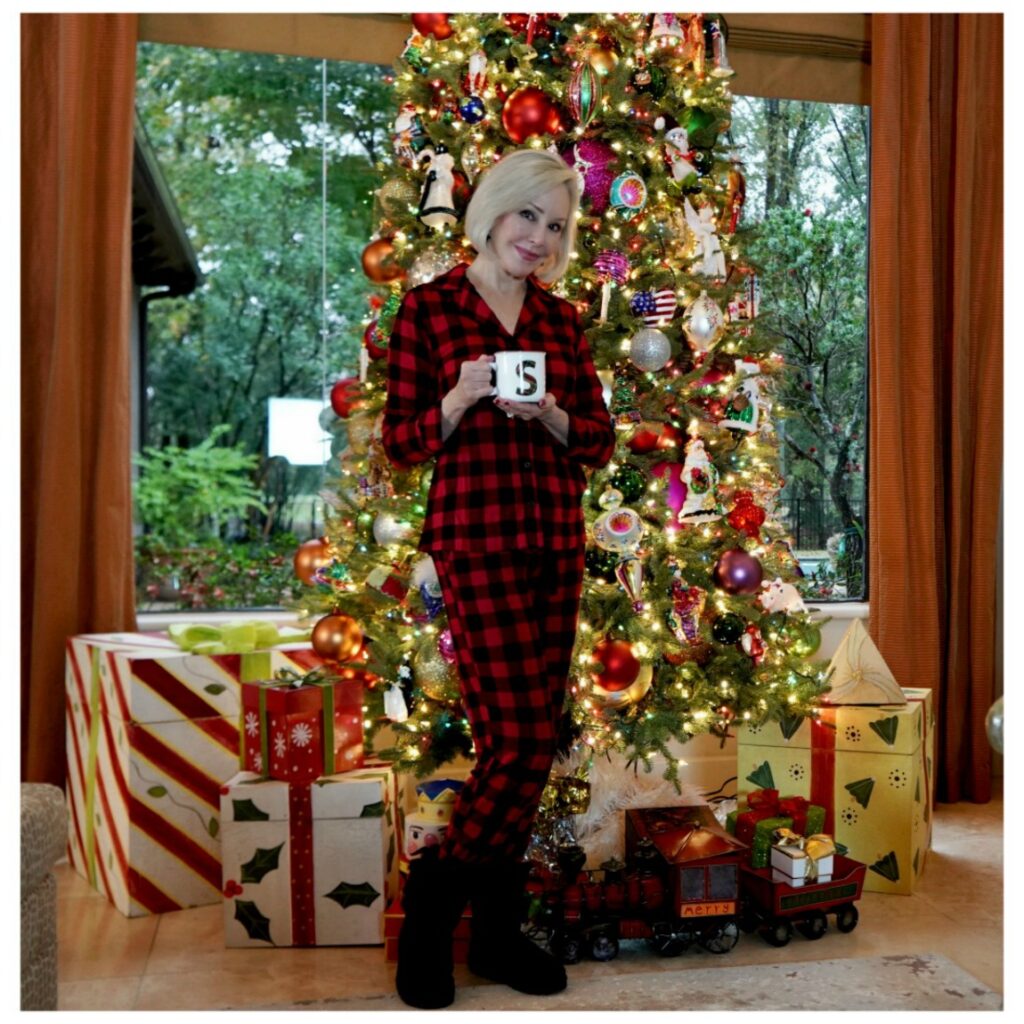 Sheree Frede of the SheShe Show standing in front of Christmas tree holding a coffee mug, wearing red and black plaid pajamas