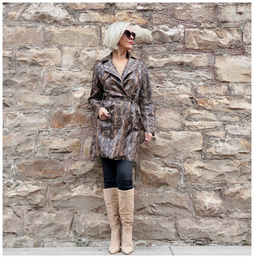 Sheree Frede of the SheShe SHow standing in front of a stone wall wearing a snakeskin print trench coat