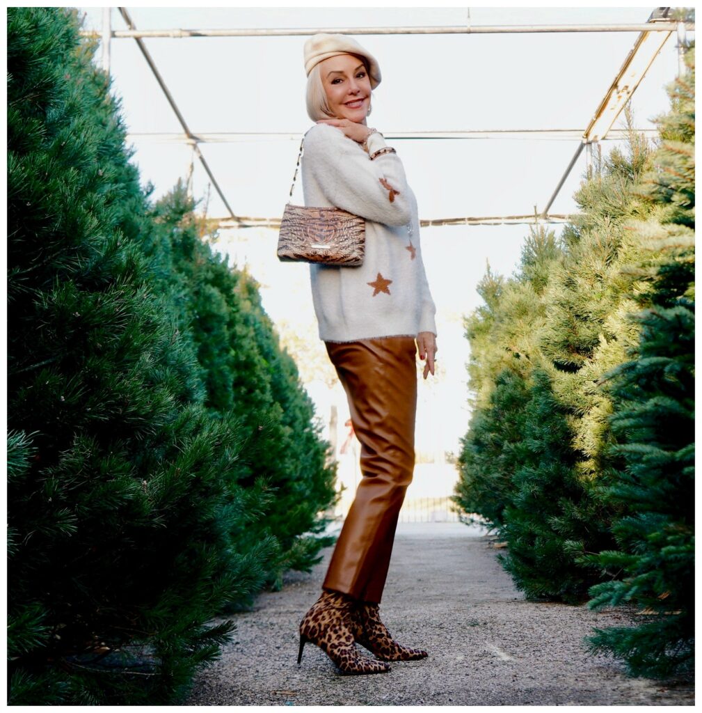 Sheree Frede of the SheShe Show standing in the Christmas tree lot wearing brown leather pants and white star sweater