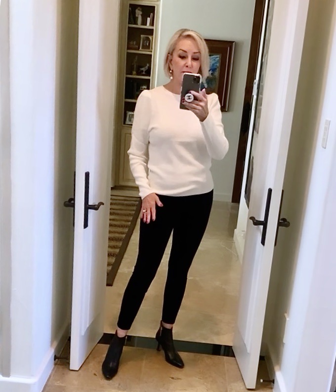 Sheree Frede of the SheShe SHow standing in front of a mirror wearing a white sweater and black pants