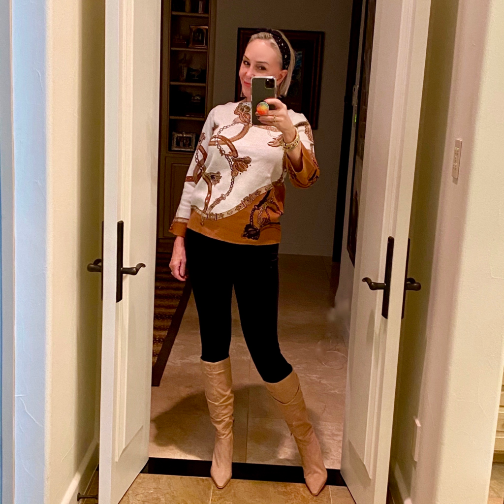 Sheree Frede of the SheShe Show standing in front of mirror wearing an equestrian print sweater over leggings and knee boots