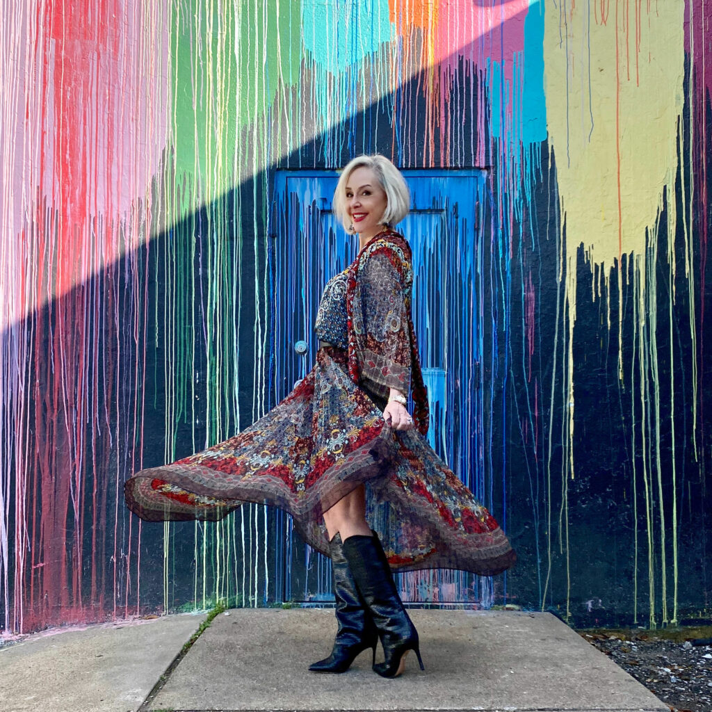 sheree Frede of the SheShe Show standing in front of paint drip mural wall wearing a flowy print skirt, knee boots