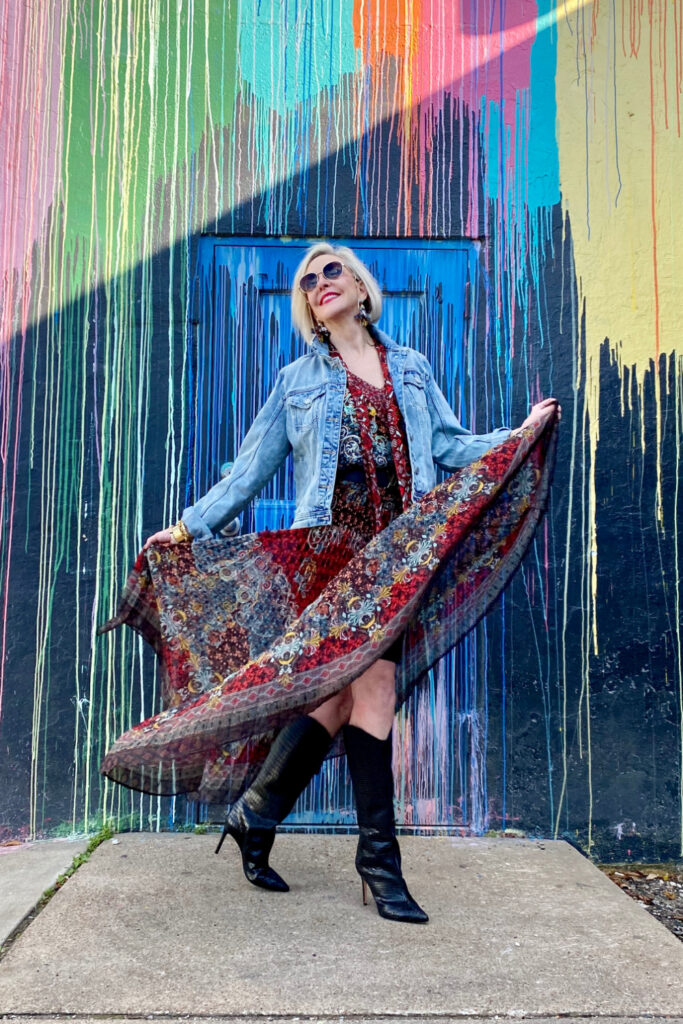 sheree Frede of the SheShe Show standing in front of paint drip mural wall wearing a flowy print skirt, knee boots and denim jacket