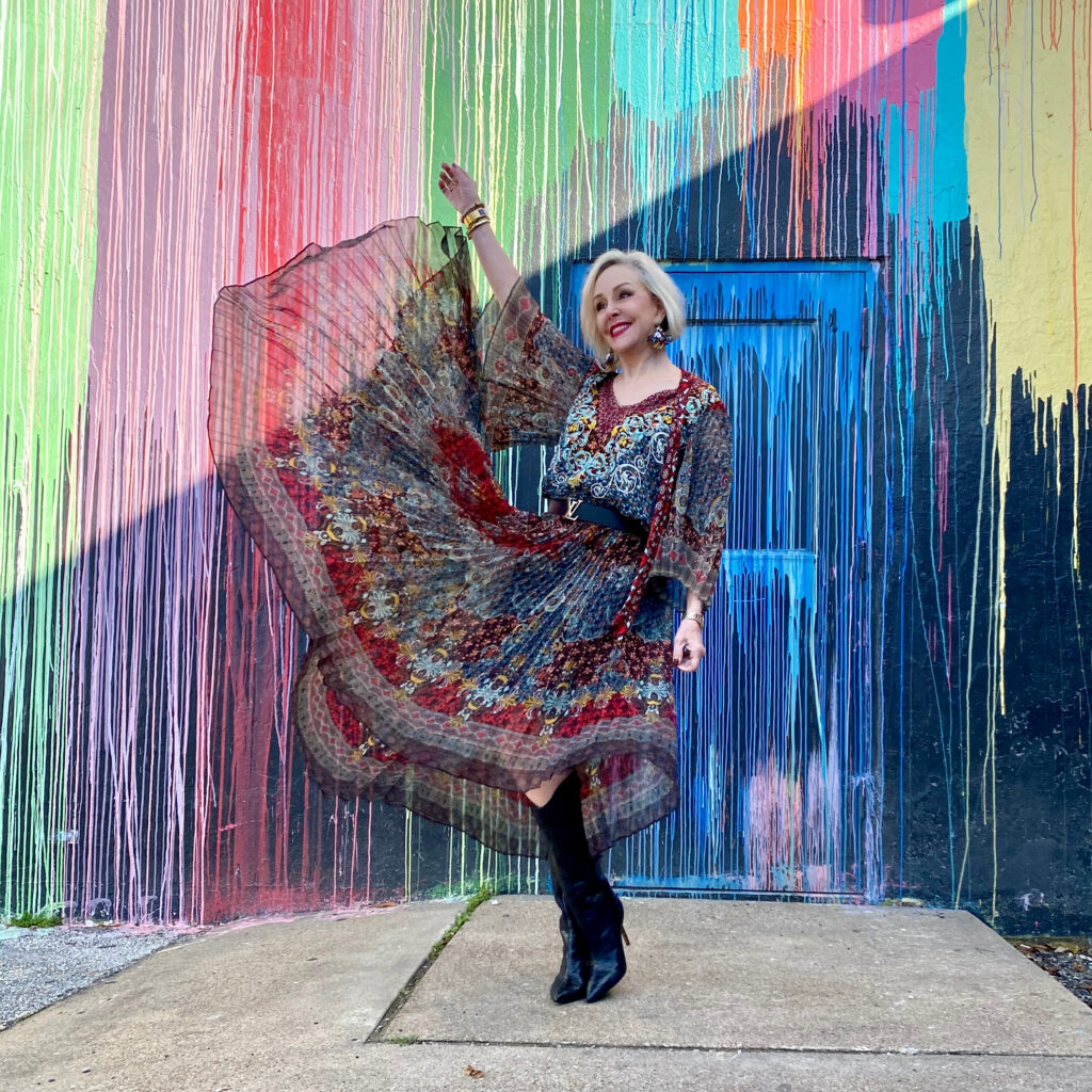 sheree Frede of the SheShe Show standing in front of paint drip mural wall wearing a flowy print skirt, knee boots  