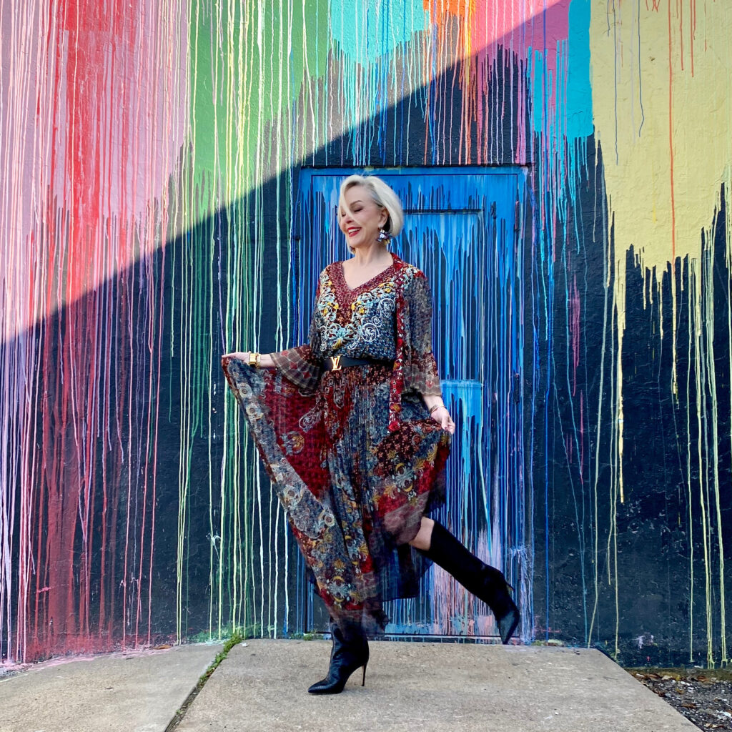 sheree Frede of the SheShe Show standing in front of paint drip mural wall wearing a flowy print skirt, knee boots