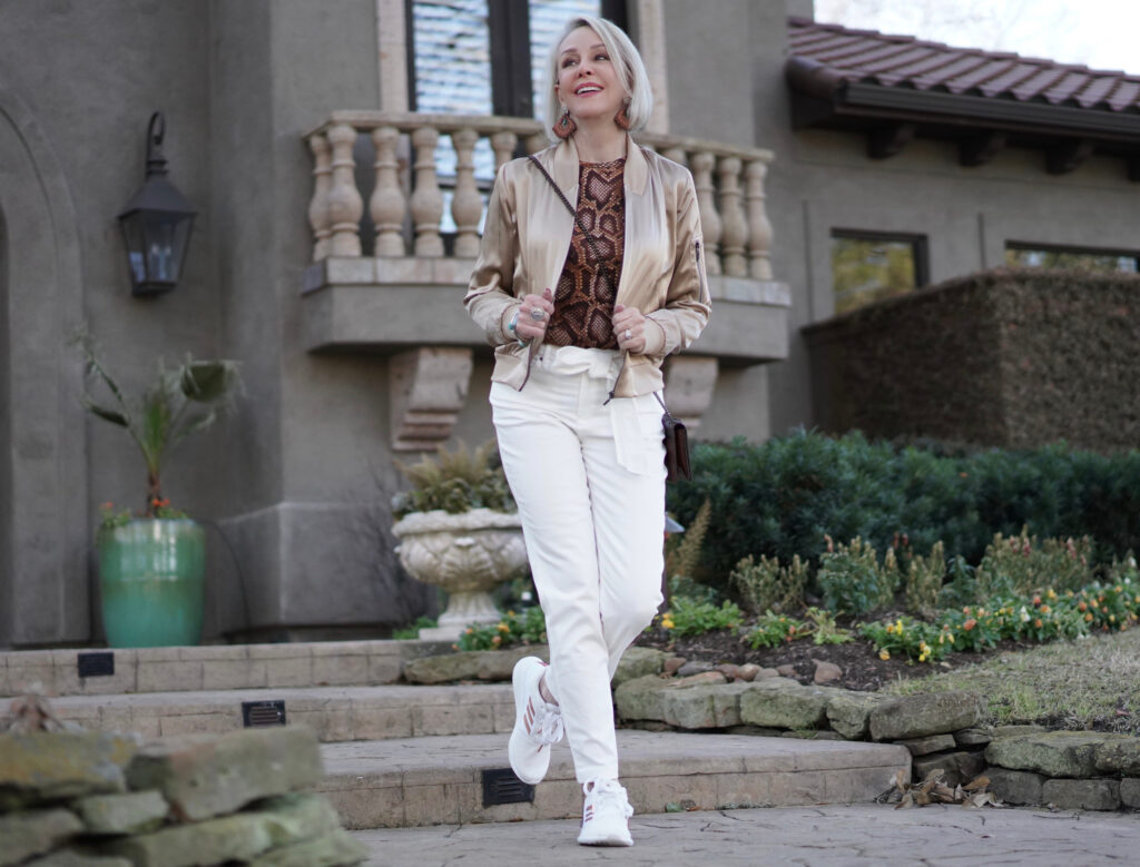 Sheree Frede of the SheShe Show white pants, gold silk bomber jacket standing in front of house