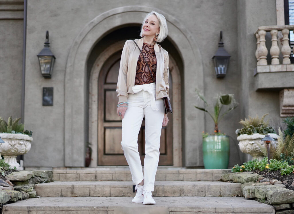 Sheree Frede of the SheShe Show white pants, gold silk bomber jacket standing in front of house