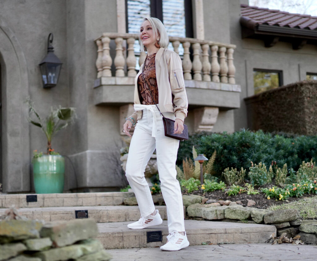 Sheree Frede of the SheShe Show white pants, gold silk bomber jacket standing in front of house