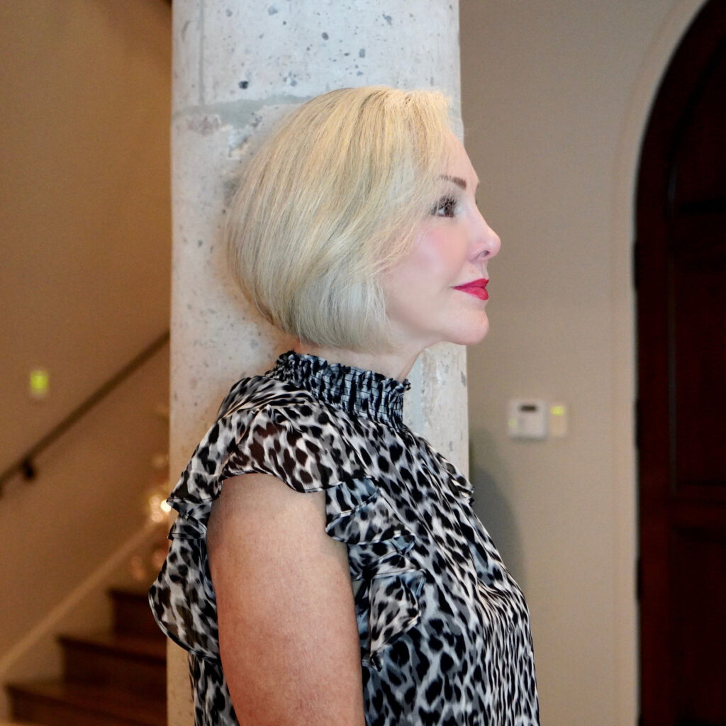 Sheree Frede of the SheShe Show standing by a stone column wearing a black and white leopard print top showing bob hairstyle