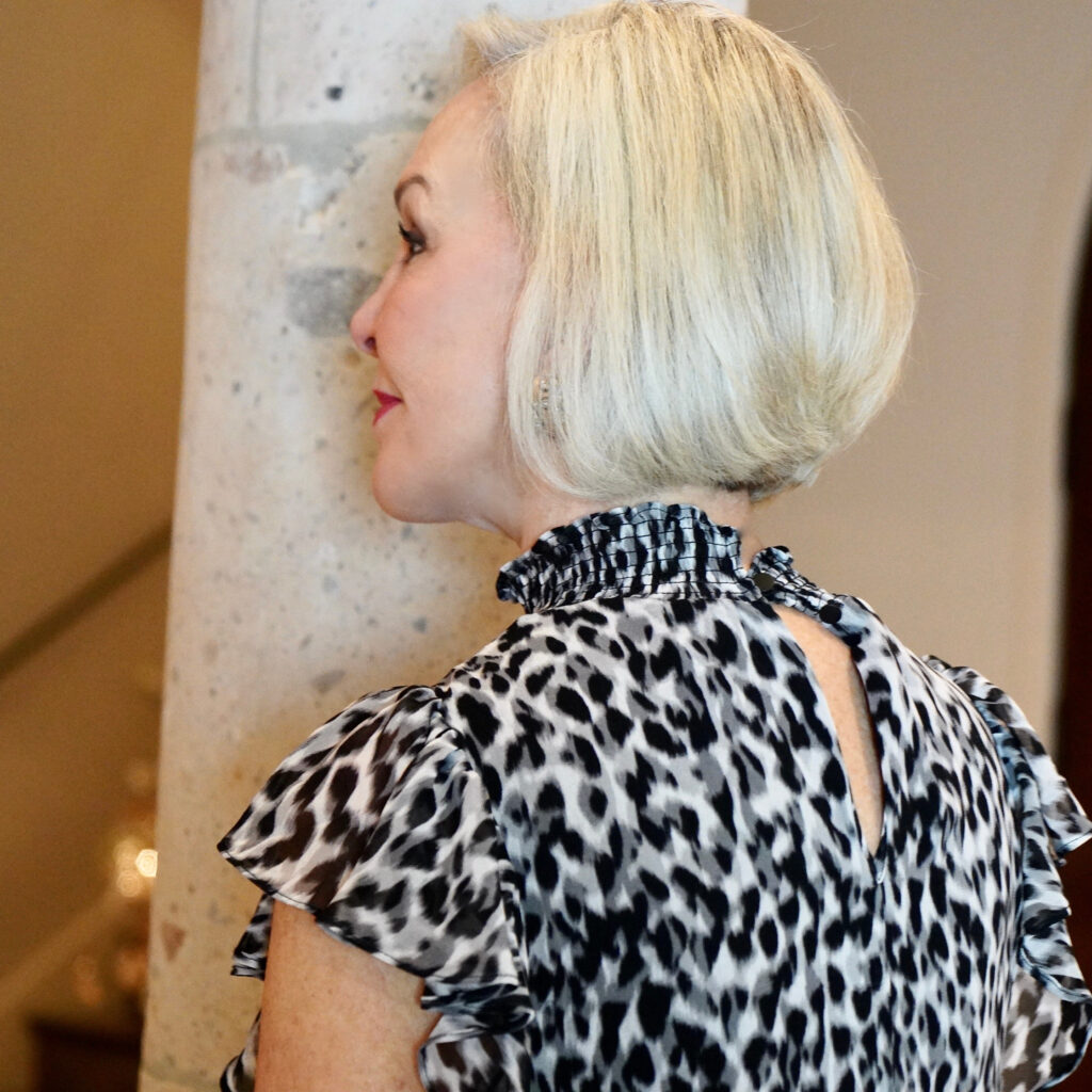 Sheree Frede of the SheShe Show standing by a stone column wearing a black and white leopard print top showing bob hairstyle
