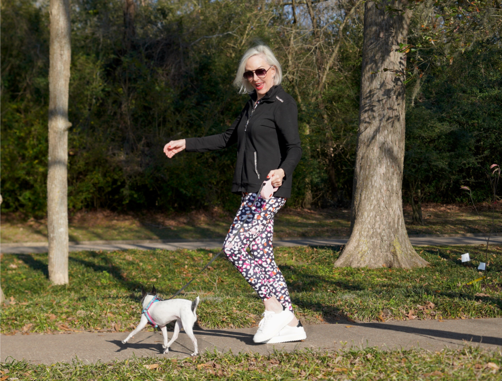 Sheree Frede of the SheShe Show walking toy fox terrrier wearing print leggings and zip knit jacket zenergy