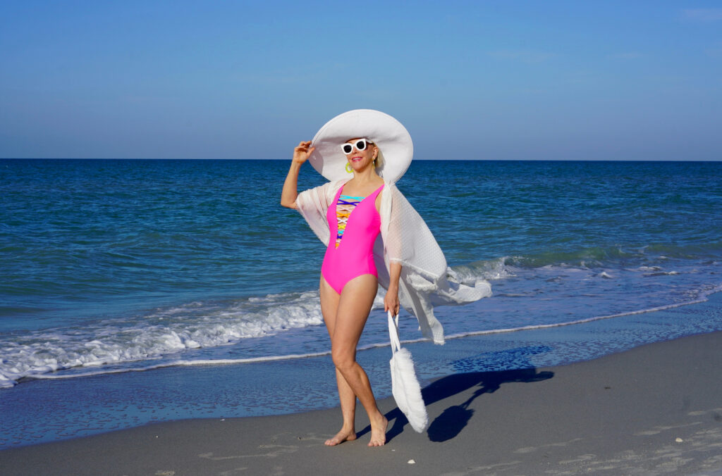 Sheree Frede of the SheShe Show in the water on the beach wearing a big hat and hot pink swimsuit
